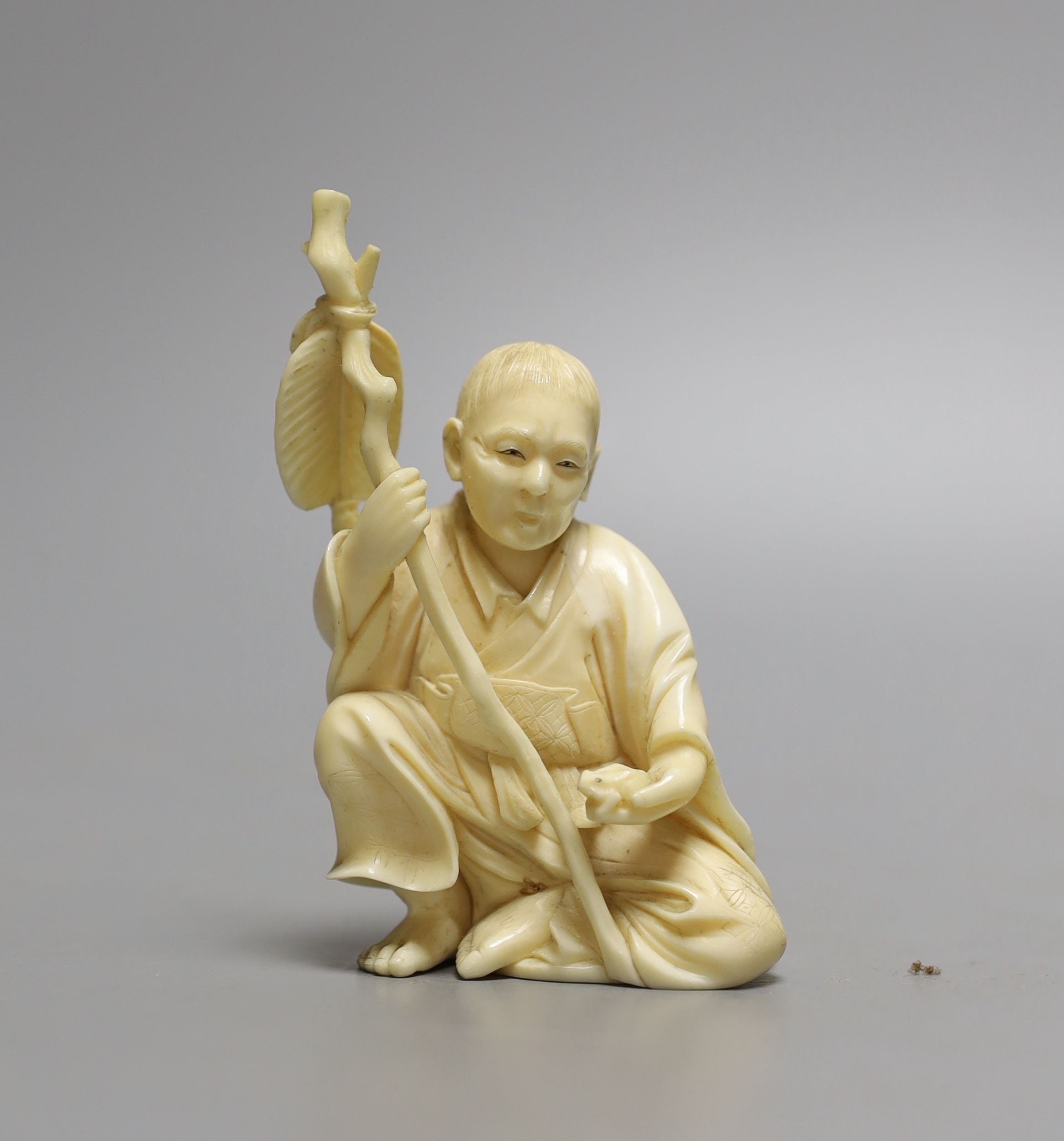 A Japanese ivory okimono of seated figure, early 20th century (possibly Gama Sennin) with paddle and holding a frog - 10cm tall